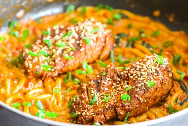 Creamy Spicy Korean Udon Noodles with Bulgogi Chicken in a pan with spring onion green garnish - front view.