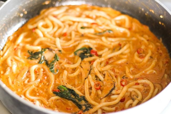 Creamy Spicy Korean Udon Noodles cooking pan with sauce, aromatics, spinach leaves, and mushroom slices