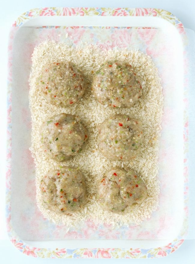 Six uncooked Thai shrimp cake patties on top of pink and white floral tray that is lined with nonstick cooking paper that has bread crumbs on top of it. 
