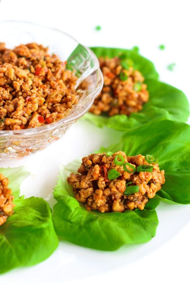 Ground chili chicken in a bowl in center of a plate surrounded by lettuce cups.