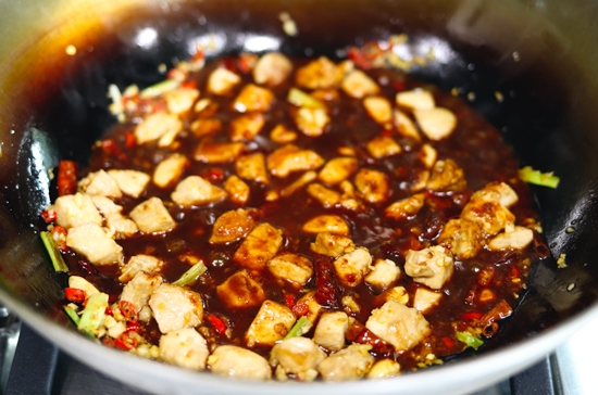 Peanuts, peppercorns, chopped red chilies, minced garlic, minced ginger, spring onion whites, diced chicken pieces and dried red chilies tossed together and simmering in spicy kung pao sauce in a wok