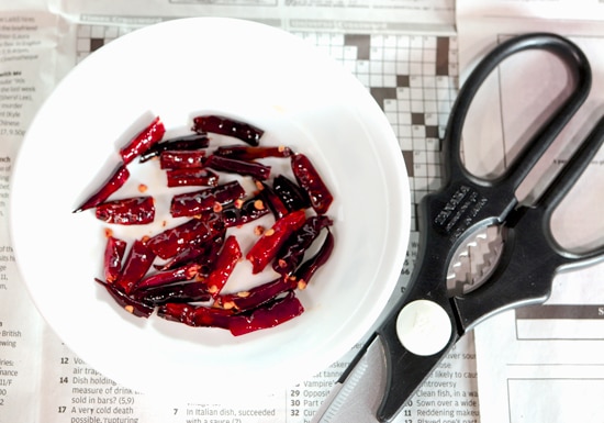 Toasted Thai Dried Chilies that have been cut up in a white bowl with kitchen scissors to the side. 
