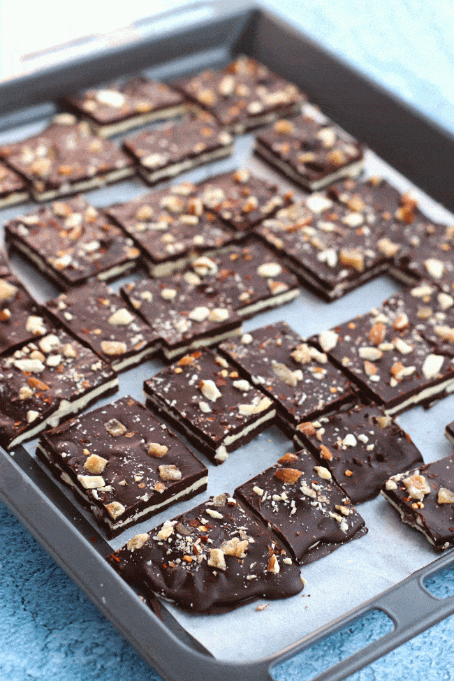 Spicy Chocolate Bark with Almonds & Candied Ginger squares on top of a sheet of nonstick cooking paper on a baking tray diagonally placed on top of a blue bubble patterned backdrop.
