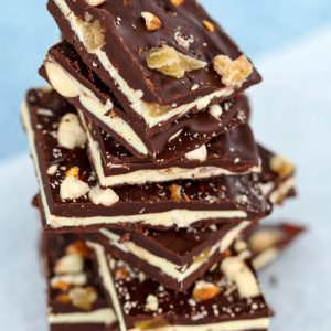 Stack of Spicy Chocolate Bark with Almonds & Candied Ginger square on a diagonally placed sheet of nonstick cooking paper on top of a blue bubble patterned backdrop.