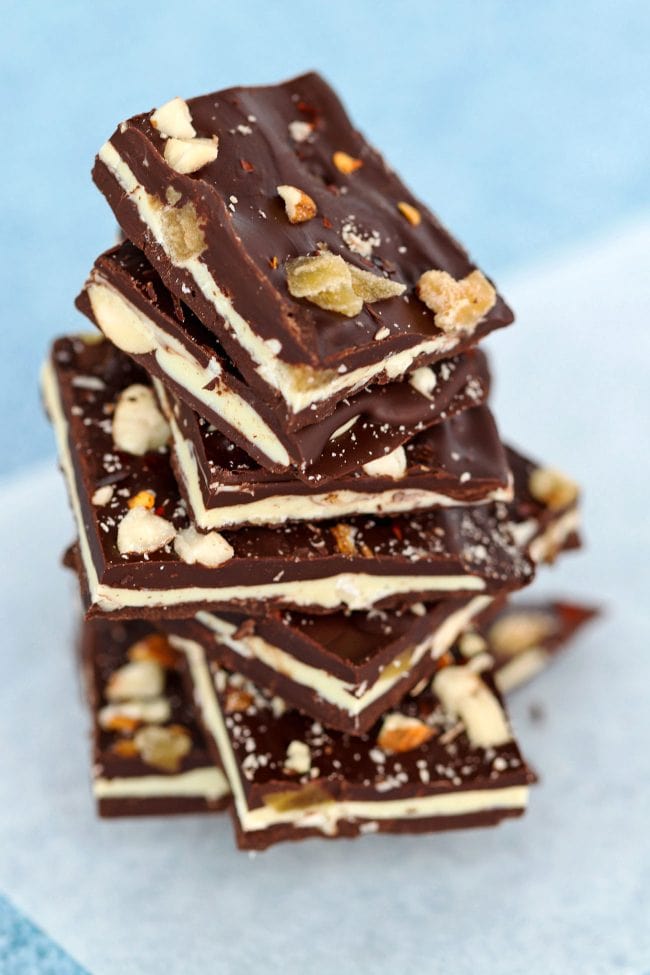 Stack of Spicy Chocolate Bark with Almonds & Candied Ginger squares placed on nonstick cooking paper on top of a blue bubble patterned backdrop.