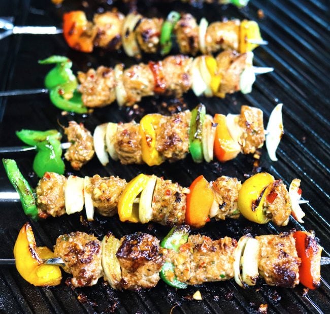 Marinated chicken pieces, diced bell pepper, and diced onion threaded on metal skewers grilling on top of Lodge's cast iron griddle on the stovetop.