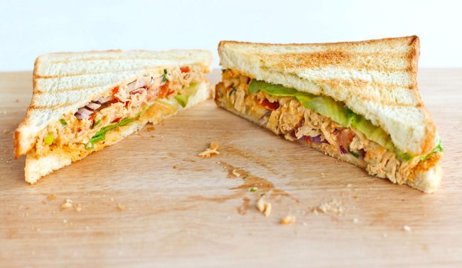 Front view of diagonally sliced Sweet & Spicy Thai Chicken Salad Sandwich on top of wooden board. 