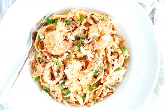 Overhead view of a deep white pasta plate with Garlic Cream Sauce Seafood Fettuccine and a silver fork sticking out of the plate on the side.