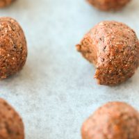 Six Nutella & Peanut Butter Energy Balls lined up on top of non-stick cooking paper. Close up and focus on one energy ball that has a bite taken out of it.