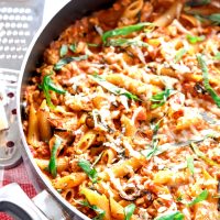 Spicy Chicken Penne Pastagarnished with grated cheese and basil leaves in a large black pan.