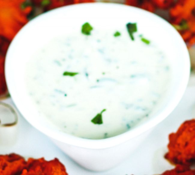 Cooling Cucumber & Mint Yogurt Dip in a white pear shaped serving bowl, garnished with fresh coriander leaves.