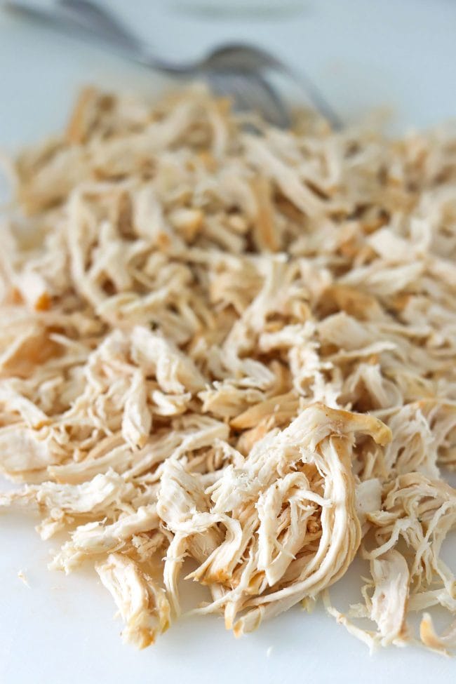 Shredded chicken on chopping board with two forks