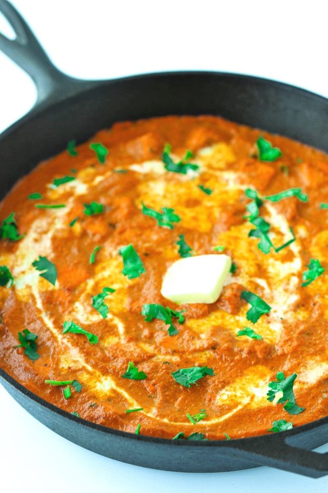 orange paneer curry garnished with coriander, cream, and butter in large black deep cast iron skillet.