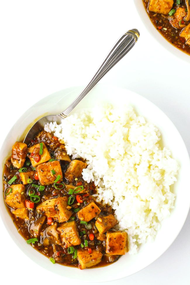 tofu in black pepper sauce on plate with rice and spoon