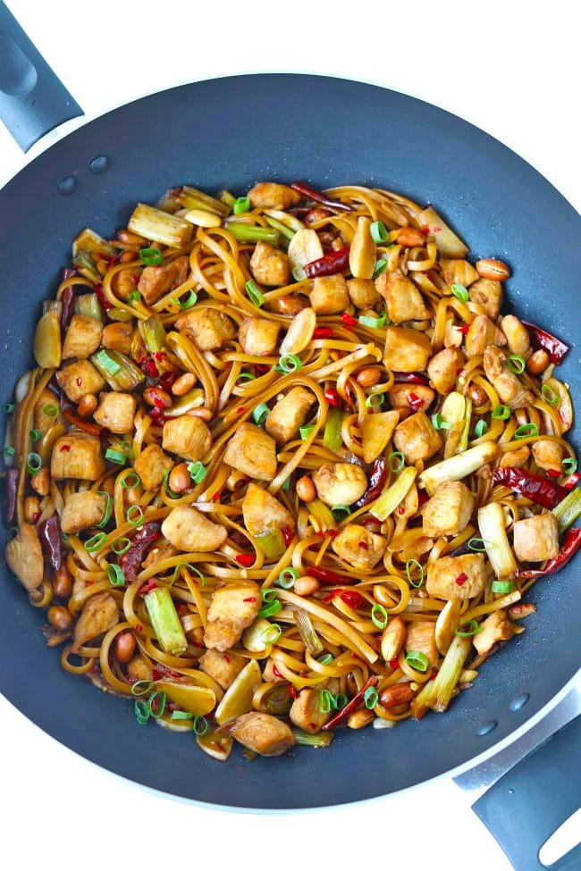 Chicken and noodles in a wok with dried red chilies, spring onion, and peanuts