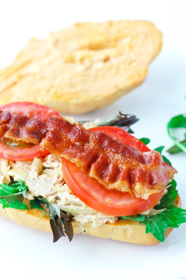 A chicken salad sandwich with spicy mayonnaise, tomato slices, mixed greens, and crispy bacon.
