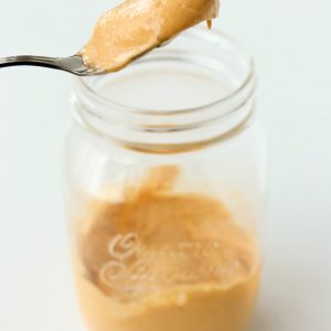 A spoon with spicy mayonnaise being held above a jar with spicy mayonnaise.