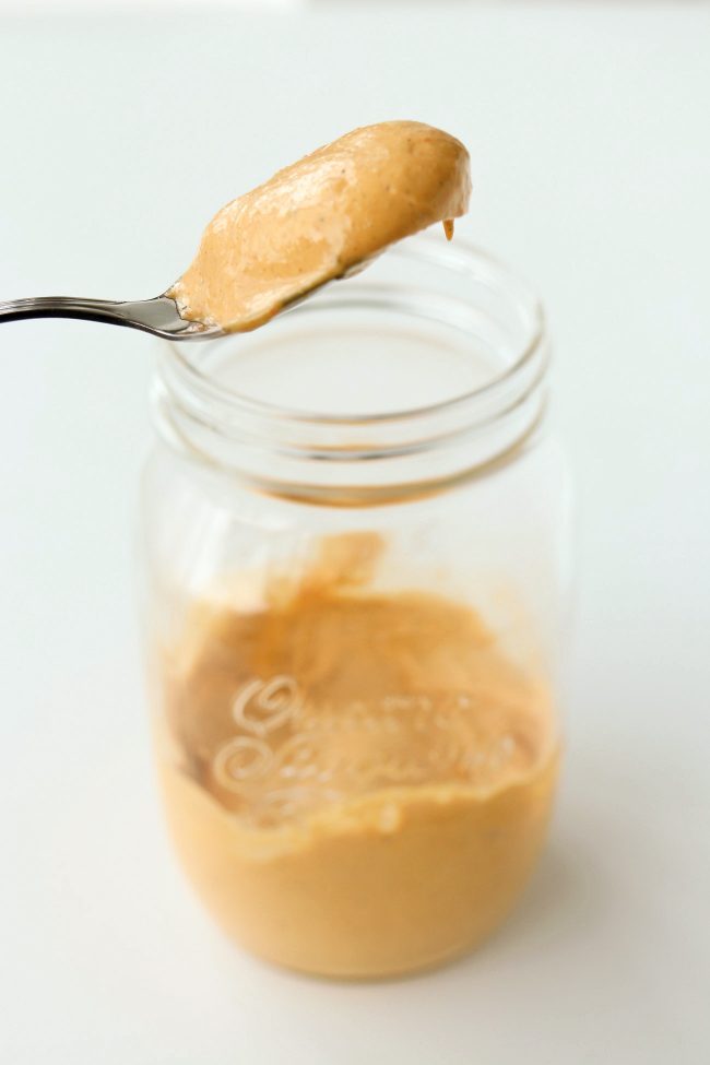 A spoon with spicy mayonnaise being held above a jar with spicy mayonnaise.