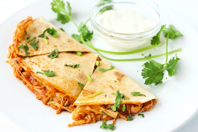 chicken quesadilla garnished with coriander and sour cream in a small dish on a plate