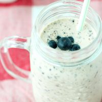 Blueberry Banana Smoothie in a mason jar mug topped with fresh blueberries, and with a straw in the mug.