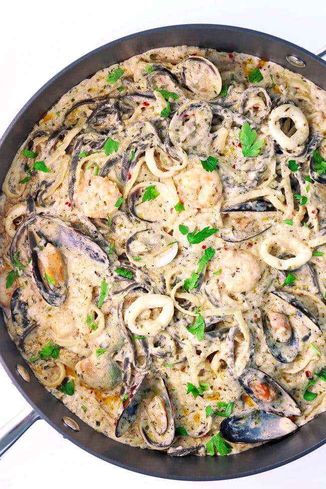 Pasta in a creamy white sauce with assorted seafood in a large deep sauté pan.