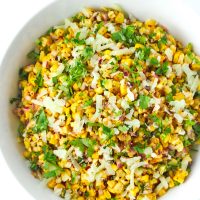 Corn salad in a white round bowl topped with grated cheese and coriander.