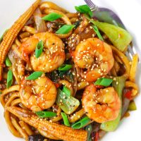 Stir-fry Sichuan Sauce Noodles with Jumbo prawns, baby corn, mushrooms, bok choy, and spring onion garnish on a plate with a fork..