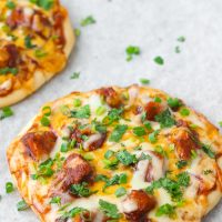 Two diagonally placed Spicy BBQ Chicken Pita Pizzas garnished with spring onion and chopped coriander
