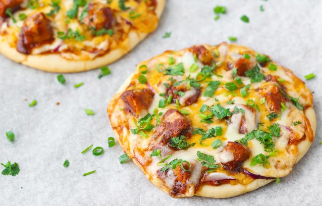 Two diagonally placed Spicy BBQ Chicken Pita Pizzas garnished with spring onion and chopped coriander.