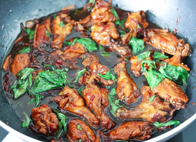 Three Cup Chicken in a wok with brown sauce and Thai sweet basil