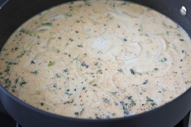Spicy Garlic Cream Sauce with sliced onion, herbs, and seasonings in a deep large sauté pan on the stovetop.