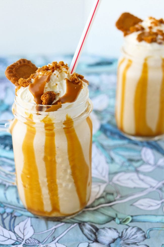 Cookie mutter milkshake in two mason jar glasses with straws, whipped cream, crumbled cookies, and melted cookie butter drizzle.
