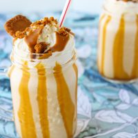 Biscoff Apple Milkshake in two mason jar glasses with straws, whipped cream, crumbled Biscoff cookies, and Biscoff spread drizzle.