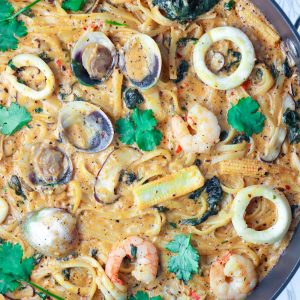 Creamy Tom Yum Pasta with clams, shrimp, squid, spinach, baby corn, mushrooms, and chopped coriander in a large black pan.