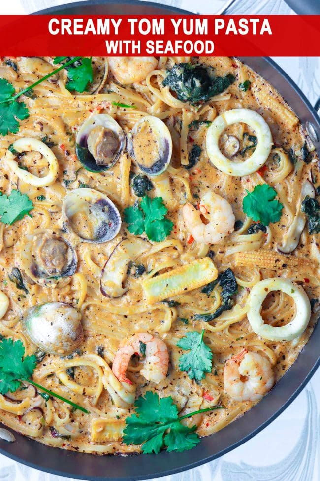 Creamy Tom Yum Pasta with clams, shrimp, squid, spinach, baby corn, mushrooms, and chopped coriander in a large pan.