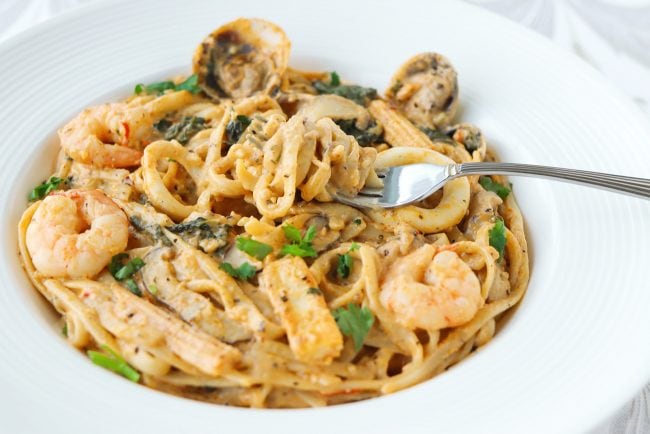 Plate with spicy orange cream sauce pasta and seafood with a fork twirled around pasta