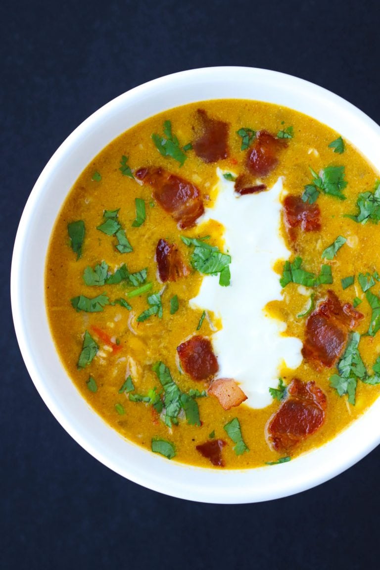 Pumpkin Chicken Soup garnished with chopped coriander, yogurt, and crispy bacon pieces in a white round bowl.