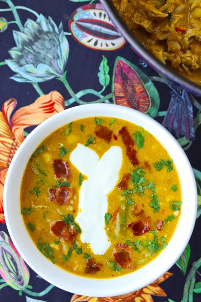 Pumpkin Chicken Soup in bowl with crispy bacon pieces, yogurt, chopped coriander. Pot with Pumpkin Chicken Soup in the back.