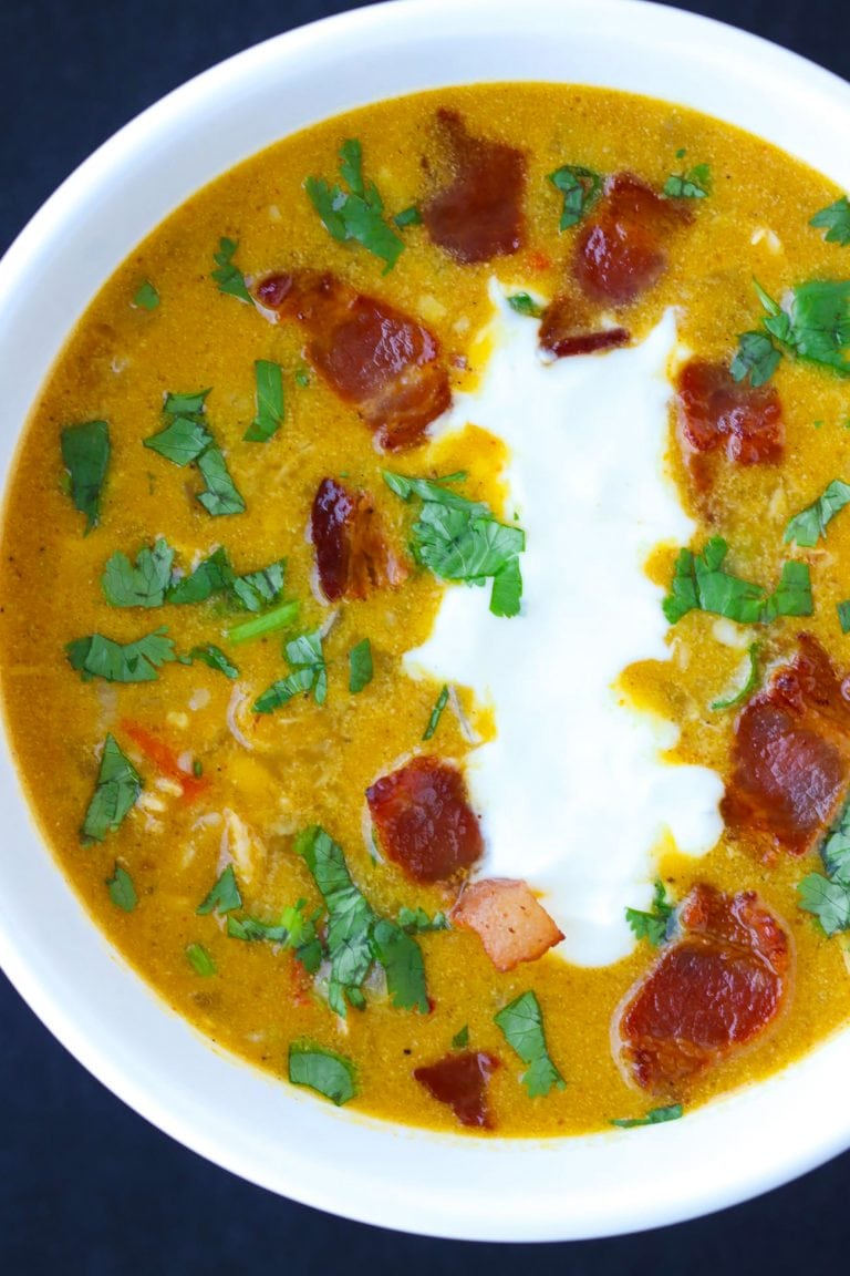 Hearty pumpkin chicken soup in a bowl topped with coriander, yogurt, and bacon pieces.