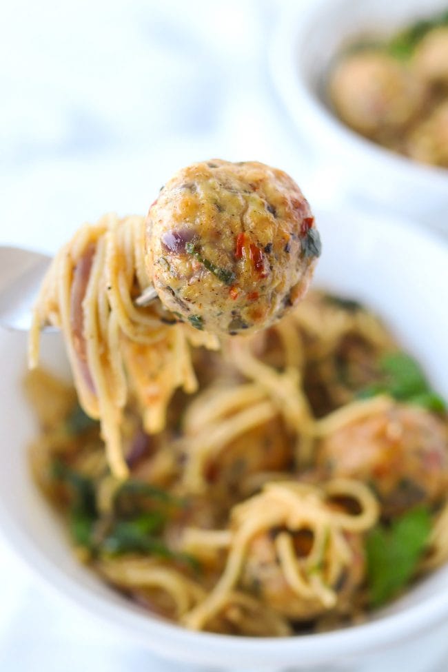 Fork holding up a bite of capellini pasta and a chicken meatball over a bowl of capellini pasta and chicken meatballs.