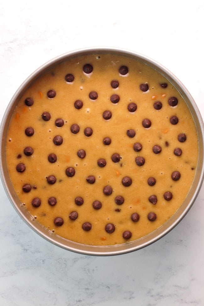 Unbaked cookie cake batter in a round 8-inch baking pan and dotted with chocolate chips.
