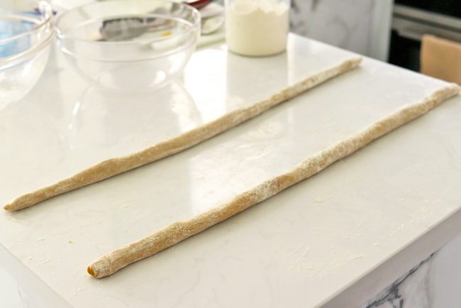 Two long thin ropes of sweet potato gnocchi dough on kitchen countertop.