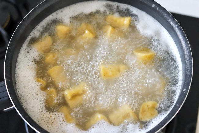 Gnocchi pieces cooking in a small pot with boiling water.