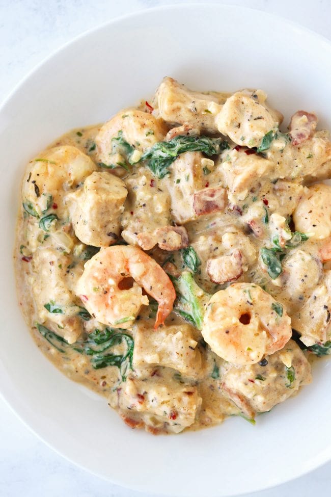 A round white plate with creamy sweet potato gnocchi with shrimp, baby kale, and bacon.