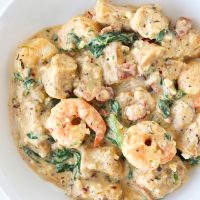 A round white plate with creamy sweet potato gnocchi with shrimp, baby kale, and bacon.