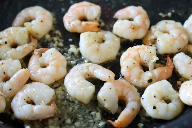 Shrimps sprinkled with black pepper cooking in a black pan with minced garlic, unsalted butter, and white wine.
