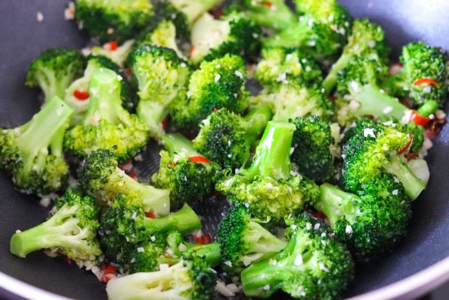 Stir-fried broccoli florets with garlic and chopped red chiles in a wok.