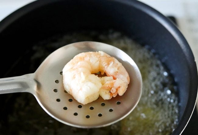 Metal slotted spoon with a deep-fried crispy prawn above a pot of bubbling oil.