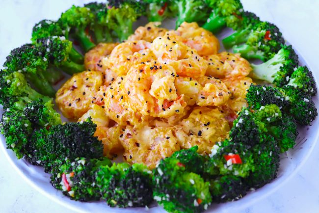 Plate lined with broccoli florets with garlic and red chilies, and mango mayonnaise coated prawns sprinkled with toasted black sesame seeds.