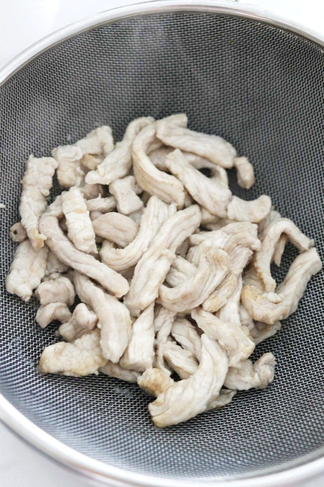 Thinly sliced starch coated blanched pork strips in a mesh strainer.